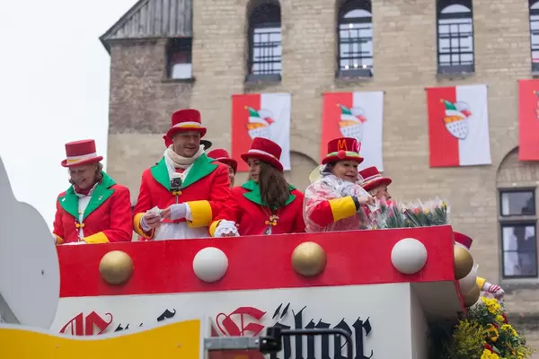 Carnival 2020 in Cologne: the float of the Große Kölner carnival society 1882 with people in red and green costumes throwing sweets and roses to the audience in front of Severinstorburg