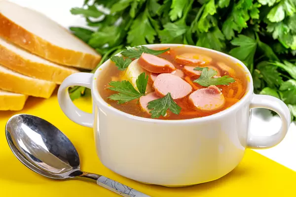 Carrot and onion soup with sausages on yellow kitchen board