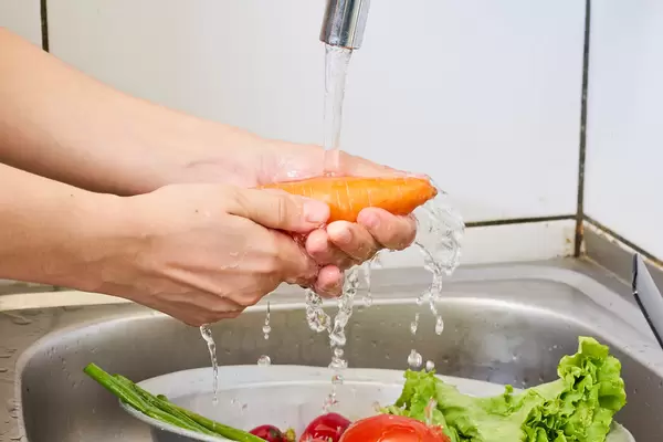 Carrots are washed under running water in a colander