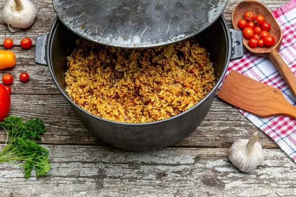 Cast iron cauldron with rice pilaf on the old wooden background (Flip 2019)