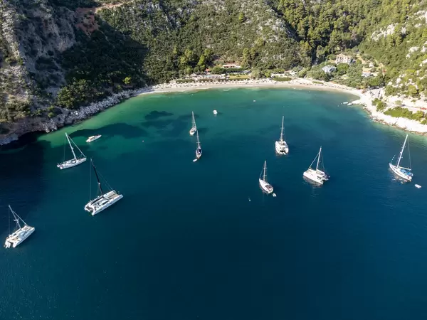 Catamarans and sailing boats in the emerald green bay of Limnonari with hills covered by pine trees