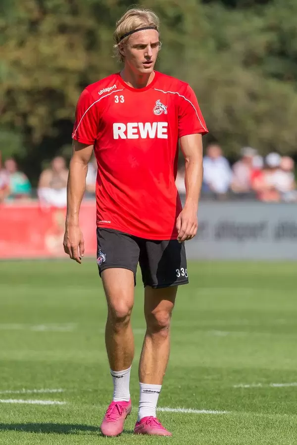 Central defender Sebastiaan Bornauw walks on the artificial turf of the football training ground, with fans in the background