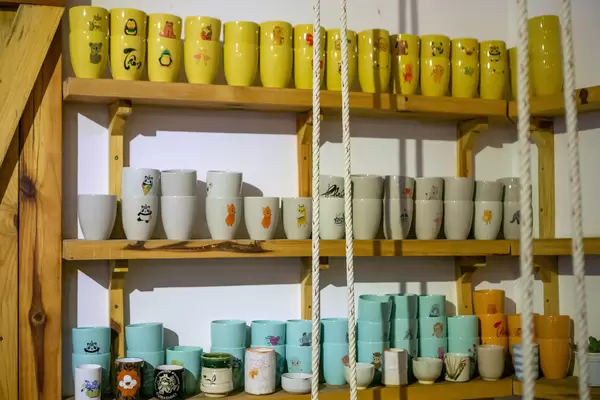 Ceramic Cups in different Colors displayed on a Wooden Shelf inside a Cafe