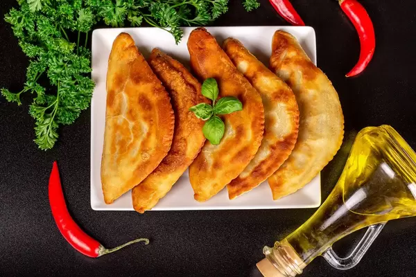 Chebureki - fried pies with meat and greens on a plate, top view