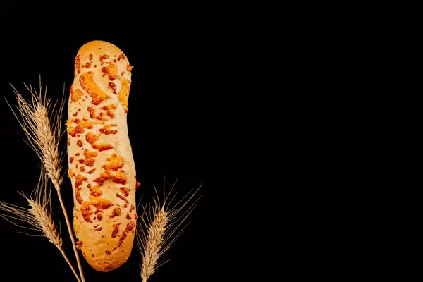 Cheese baguette on a black background with wheat spikelets, top view