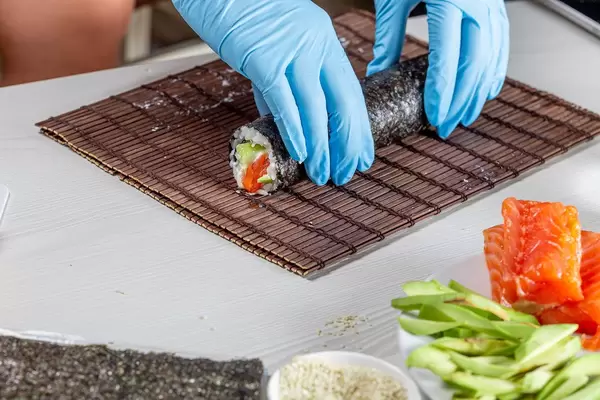 Chef hands in disposable gloves cooking sushi at kitchen of home