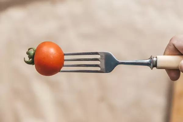 Cherry-Tomate auf einer Gabel aufgespießt, vor braunem Backpapier