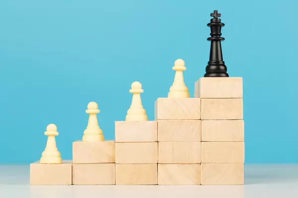 Chess standing on a ladder of wooden building blocks with the king at the top