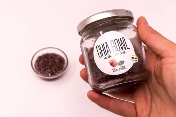 Chia Bowl - Chiapudding mit Apfelaroma in Glas von Hand gehalten und Schale im Hintergrund