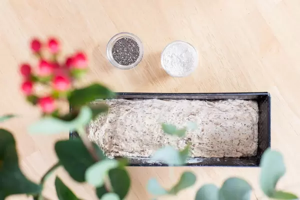 Chia bread dough in a loaf pan and flour and chia seeds in small glass dishes