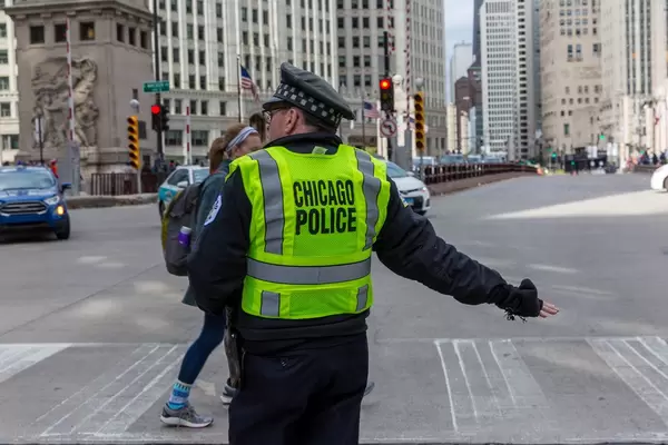 Chicago police officer with a yellow vest at an intersection in Downtown Chicago while a woman crosses the road