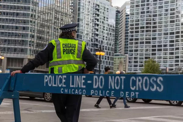 Chicago Polizist steht neben einem blauen hölzernen Barriere mit Schriftzug "Police line - Do not cross. Chicago Police Dept"