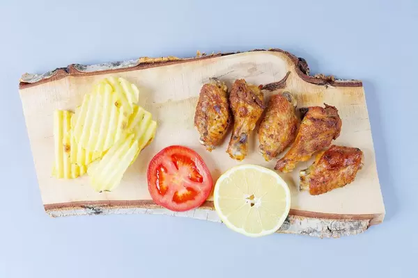 Chicken wings with potato chips on a wooden chopper (Flip 2019)