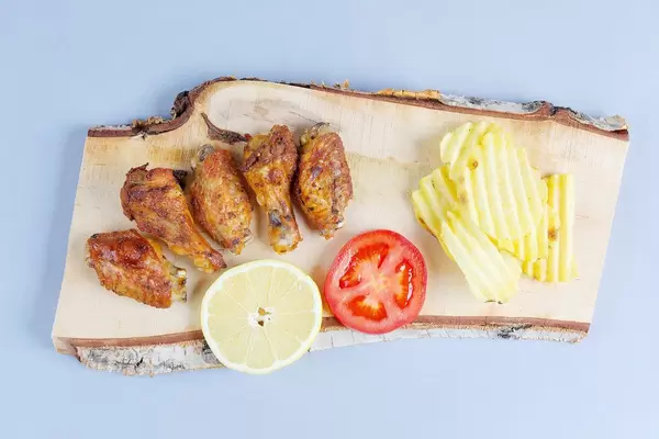 Chicken wings with potato chips on a wooden chopper