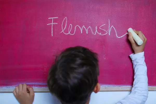 Child writes Flemish word on chalkboard, learning foreign language