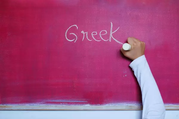 Child writes Greek word on chalkboard, learning foreign language