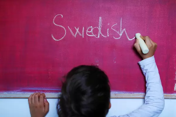 Child writes Swedish word on chalkboard, learning foreign language