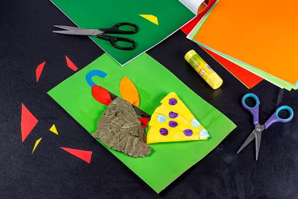 Children's handicraft with colored paper, glue and scissors on a black background