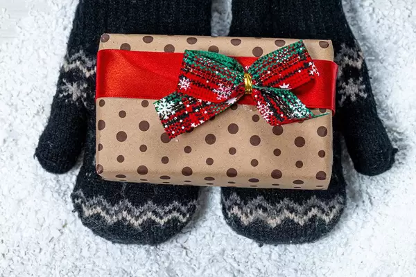 Children's hands in mittens are holding a gift on a snow background. View from above (Flip 2019)