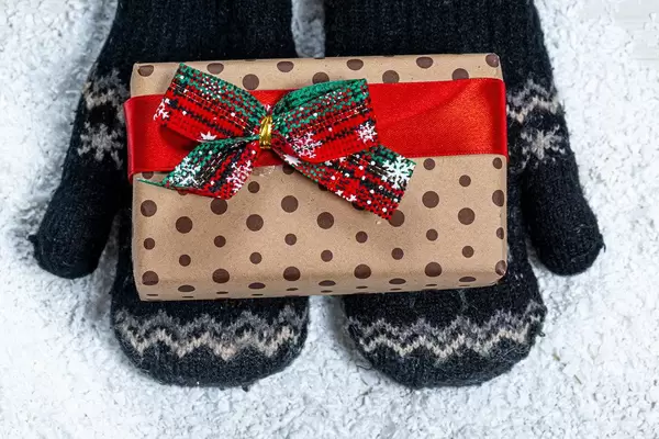 Children's hands in mittens are holding a gift on a snow background. View from above