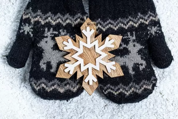 Children's hands in mittens hold a wooden snowflake on a background of snow. Winter concept