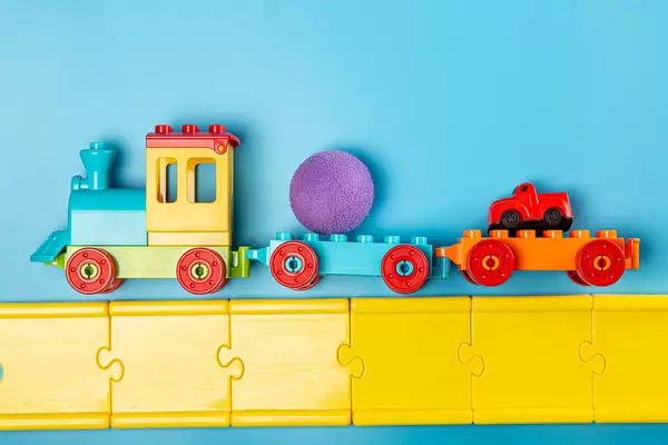 Children's plastic constructor steam locomotive with toys and road on blue background