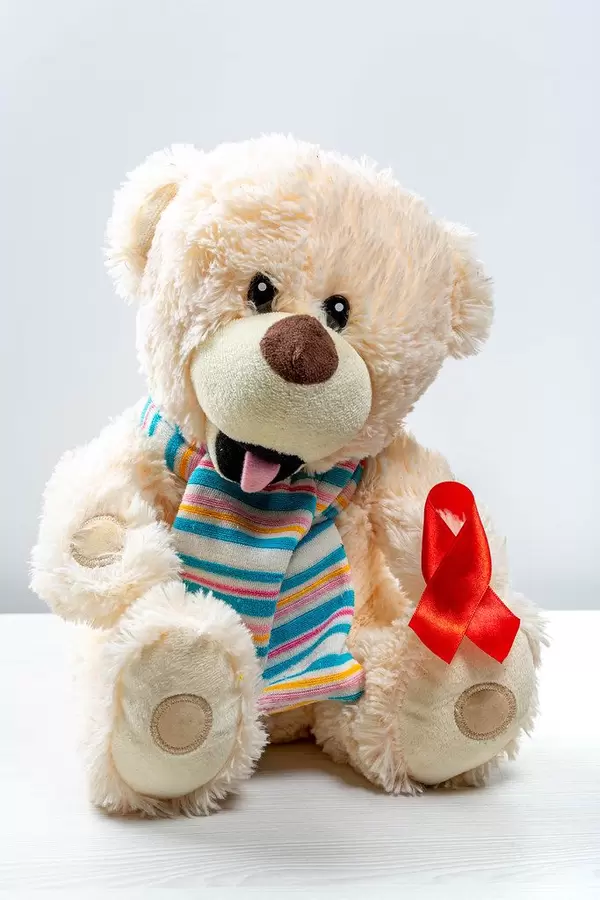 Children's toy bear with red ribbon as a symbol of the fight against children's cancer
