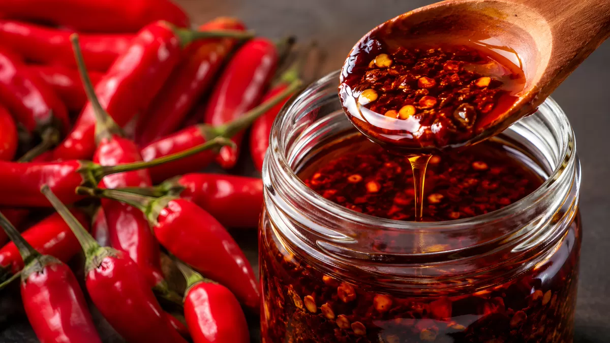 Chiliöl im Glas neben frischen roten Chilischoten