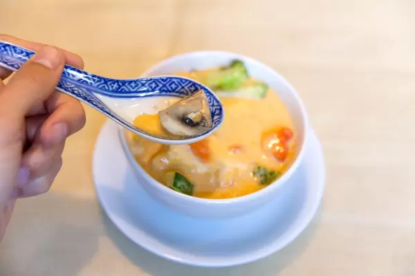 China spoon in a men's hand Asian coconut milk soup Tom Yum with tofu, hot spices and healthy vegetables for a meatless meal