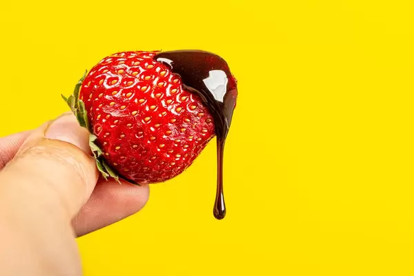 Chocolate drips from fresh strawberries on a yellow background