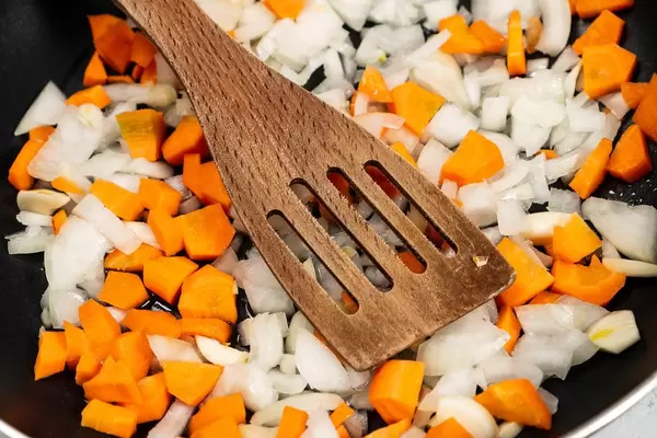 Chopped Carrots and Onions in the frying pan with wooden spoon (Flip 2020)