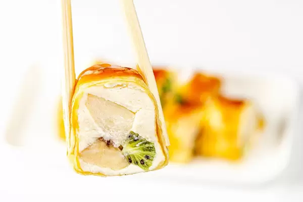 Chopsticks hold a dessert roll with cheese, Apple, kiwi and banana (Flip 2020)