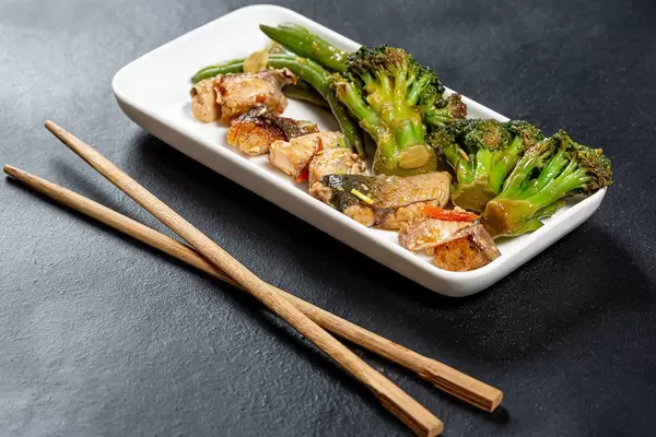 Chopsticks on black background and white plate with tuna slices and vegetables