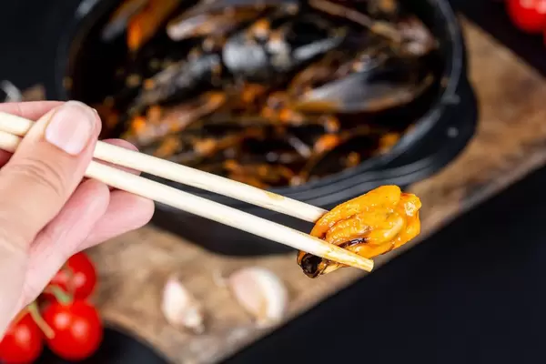Chopsticks with mussels in a woman's hand