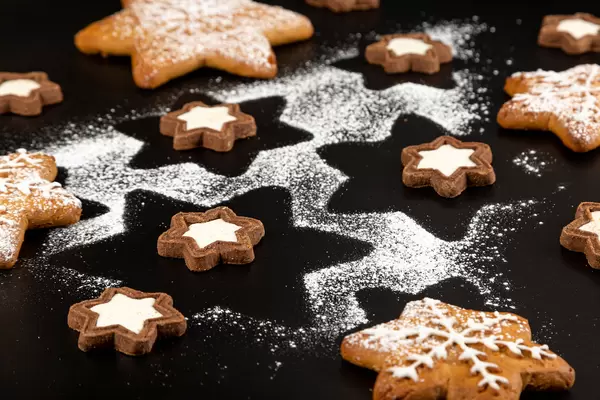 Christmas background with gingerbread, cookies and powdered sugar on black background