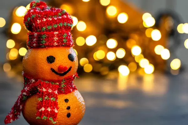 Christmas background with snowman made from tangerines and bokeh luminous garlands