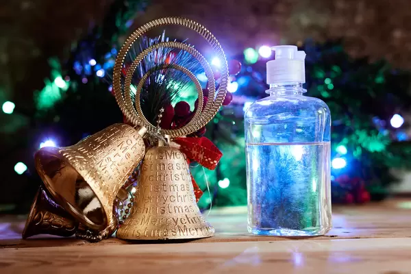 Christmas bell and bottle of antiseptic gel over decorated festive tree