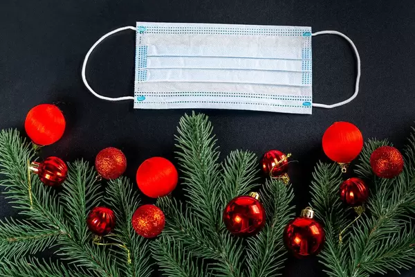 Christmas decor, balls and branches of a Christmas tree on a black background with a medical mask