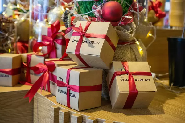 Christmas Gift Boxes with Red Ribbon on a Wooden Table with Decorated Christmas Tree and other Decorations in the Background