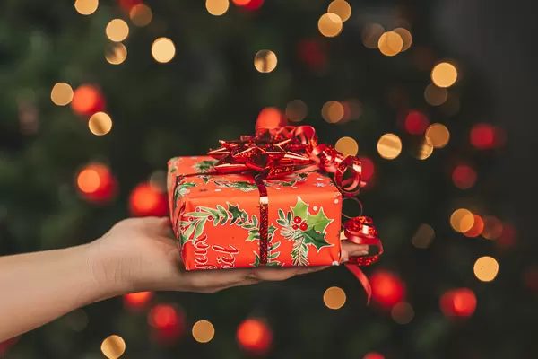 Christmas gift held in a hand by a christmas tree
