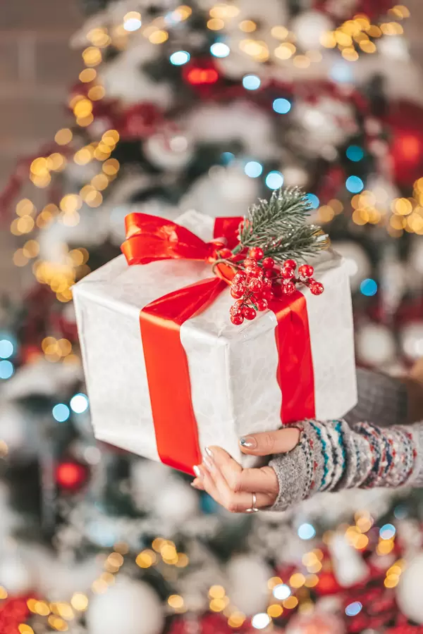 Christmas gift with red ribbon in hands on multicolored bokeh background