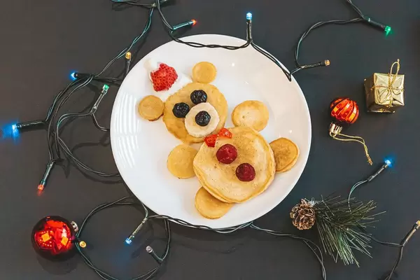 Christmas kids breakfast with bear pancakes and garland on dark background