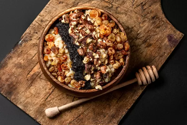 Christmas porridge with raisins, poppy seeds, walnuts and honey in a wooden bowl, top view
