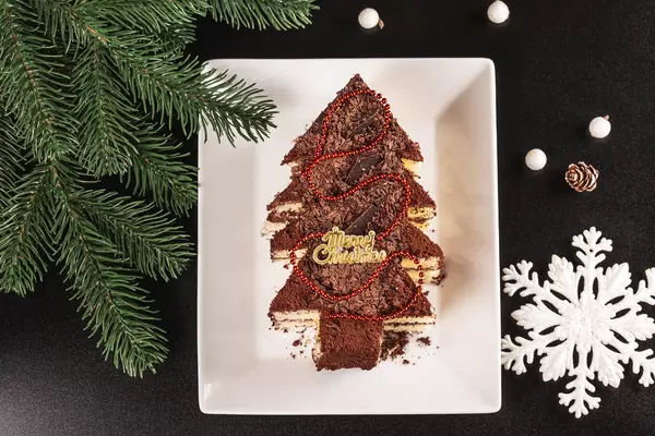 Christmas tree cake on a dark background with Christmas tree branches and a snowflake