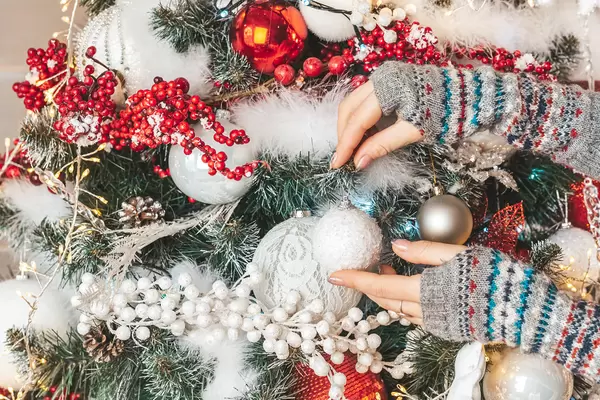 Christmas tree decoration, female hands hangs a ball on a branch