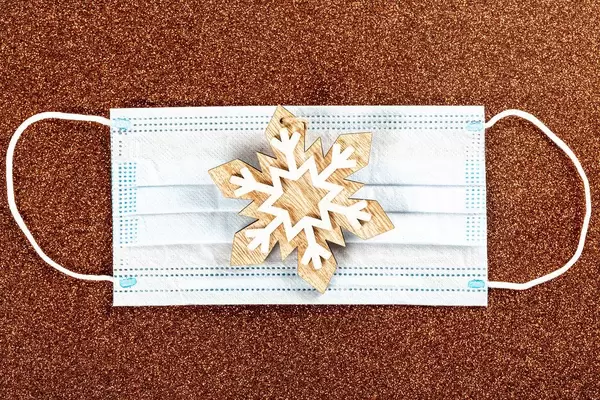 Christmas wooden toy, snowflake and medical mask on brown background, top view