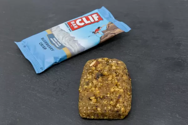 Clif Bar -  Energieriegel mit Blaubeeren-Knusper Geschmack und Verpackung auf schwarzem Hintergund
