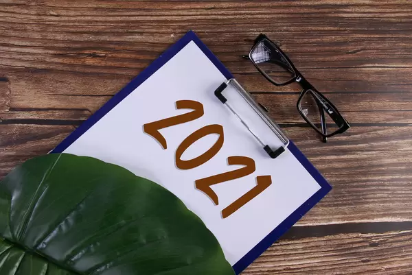 Clipboard with 2021 text and glasses on wooden table