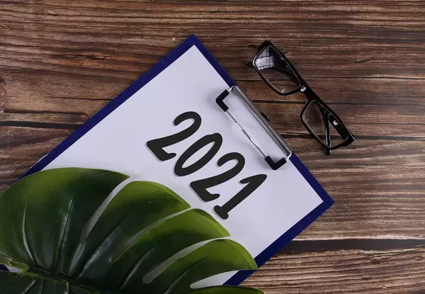 Clipboard with 2021 text and monstera leaf on wooden table