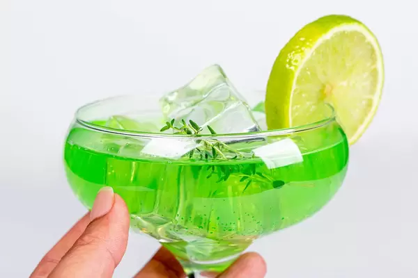 Close-up, a glass of green cocktail with lime in a woman's hand